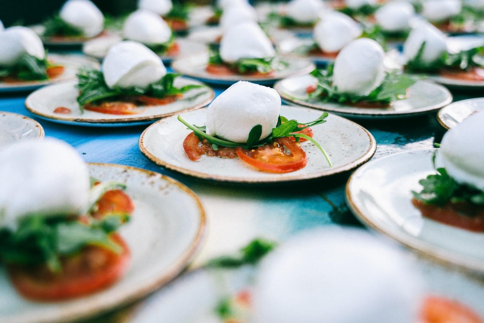 Plates of fresh mozzarella balls served with tomato slices and arugula on a dining table.